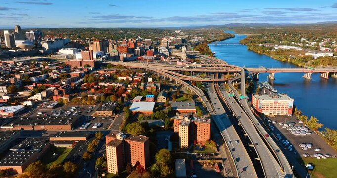Big interchange with highways, loops and freeways near the waterscape of the river and bridge across it. Sunlit panorama of Albany, New York, USA along the Hudson River. Aerial view.