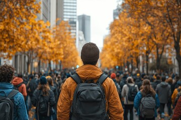 A lone man with a backpack walks through a crowd of people in a city street lined with autumn trees.