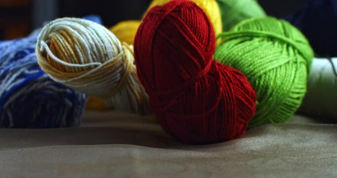 Super slow motion close up of vibrant colors warm soft and fluffy wool yarn balls are falling on wooden table in artisan handmade and handicraft creative artistic workshop at 1000 fps.