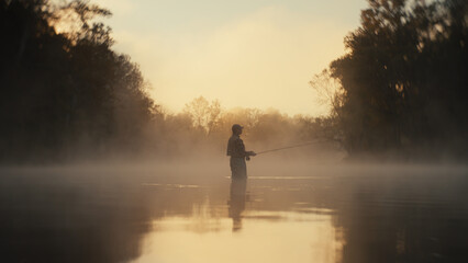 Young fly fisherman casting on a foggy river at sunrise