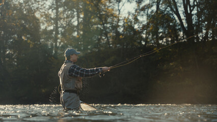 Young fly fisherman casting on a foggy river at sunrise