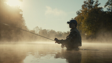 Young fly fisherman casting on a foggy river at sunrise