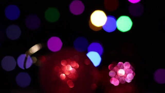 Una toma de cerca de dos bola de navidad roja desenfocada rodeada de luces de varios colores con un fondo desenfocado.  Decoraci&oacute;n de navidad y fin de a&ntilde;o.