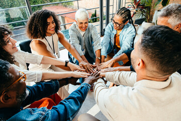 Diverse group of people coming together, placing hands in unity during a team building session in a...
