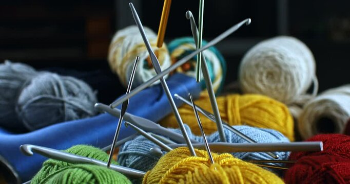 Super slow motion close up of knitting accessories such as crochet hooks and knitting needles are falling on vibrant wool yarn balls at crafting art workshop studio at 1000 fps.