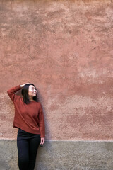 Beautiful oriental woman standing against a textured weathered pastel coloured wall and looking up towards the left