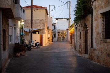 Narrow Greek streets in Hersonissos, Crete, Greece, lined with charming whitewashed buildings, colorful flowers, and vibrant local shops, exuding charm.