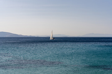 Fototapeta premium A sailing boat in the open and calm Mediterranean Sea. Alone boat in the ocean. Blue Water. White Sail.
