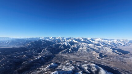 Aerial view of a serene mountain range with snow-capped peaks under a clear blue sky.