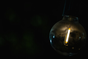 A close-up of a glowing vintage-style light bulb with a warm amber glow in a dark, moody setting....