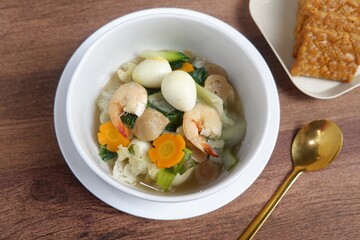 Capcay, stir-fried vegetables with meatballs, shrimp and eggs. Served on a white bowl.