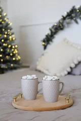 Two gray cups with cocoa and colored marshmallows on the bed © Tetiana