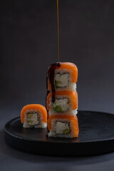 Stack of sushi rolls drizzled with soy sauce on a black plate in a minimalist setting. Concept of Japanese cuisine, fresh ingredients and food presentation. Vertical photo