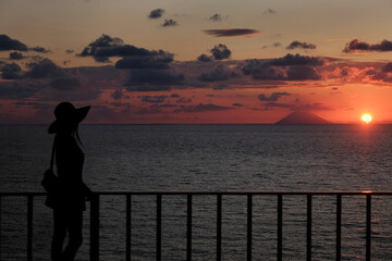 Fototapeta premium Woman silhouette enjoying sunset over stromboli volcano from a balcony