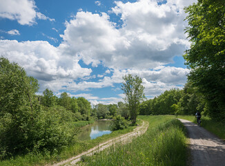 Mangfall river and green riverside with trees, bike wy with biker. blue sky with clouds