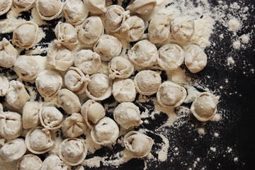Raw dumplings, top view, flat lay. Cooking dumplings. Meat dumplings or ravioli on dark background. Slavic traditional dish. Food background. Dumplings rolled in flour