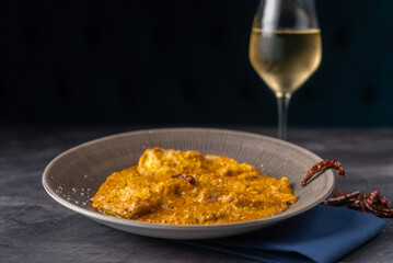 Curry with pieces of succulent chicken garnished with herbs and spices served in a textured bowl. beside it, a glass of crisp white wine.