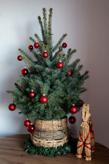 A Scandinavian-inspired Christmas display featuring a red-decorated artificial tree in a straw pot, accompanied by a traditional Yule Goat.