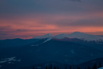 A fiery sunset paints the sky above a majestic mountain range against a breathtaking twilight sky