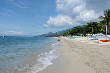 A tropical beach with palm trees, white sand, blue sky, and traditional fishing boats on the shore. Amazing beach scene vacation and summer holiday concept. Luxury travel