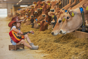 Charming child in a cowboy costume sings for cows on a farm in Denmark