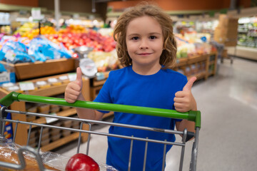 Kid with shopping cart at grocery store. Child choosing fruits and vegetables during shopping at vegetable supermarket.