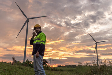 Professional Man Maintenance engineers working in wind turbine farm at sunset. Engineer Man standing among Wind Energy Turbine.