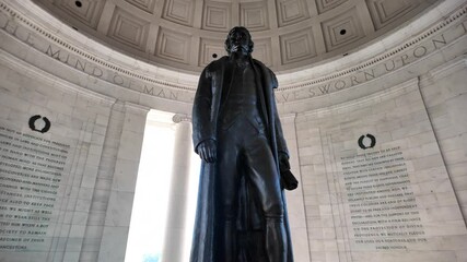 A black statue of Thomas Jefferson stands in the interior of the Jefferson Memorial, facing the inscription I Have Sworn Upon The Mind Of, surrounded by white marble walls, Washington DC. - Powered by Adobe