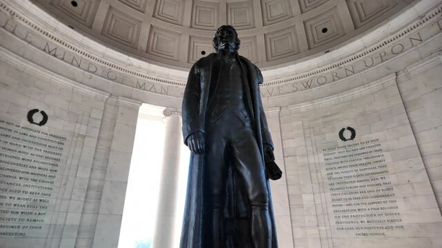 A black statue of Thomas Jefferson stands in the interior of the Jefferson Memorial, facing the inscription I Have Sworn Upon The Mind Of, surrounded by white marble walls, Washington DC.