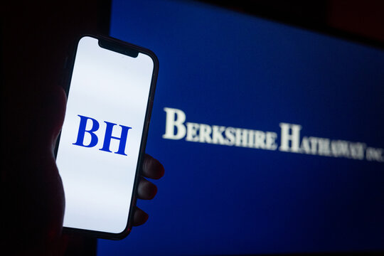 Silhouette of Hand Holding iPhone with Berkshire Hathaway Logo in Front of Computer Screen Displaying Logo &ndash; Multinational Conglomerate Holding Company &ndash; Berkshire Hathaway Inc. (BRK.A / BRK.B)