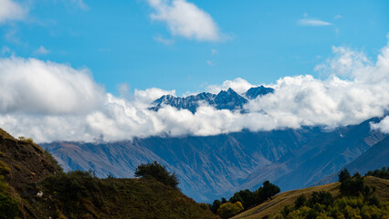 Mountains, the tops of which are surrounded by swirling clouds against a blue sky background