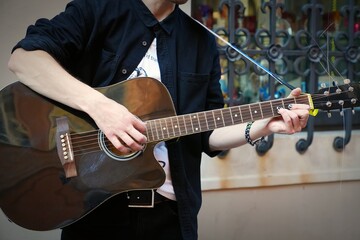 A young male with a beard and black hair plays an acoustic guitar outdoors. The scene features a reflective surface with artistic patterns, contributing to a serene atmosphere.