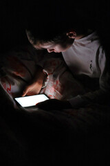Kid sitting in bed at night with his smartphone on