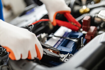 A mechanic connects jumper cables to a car battery in a garage during daytime, ensuring proper...
