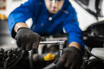 A mechanic working diligently on a car engine while using a ratchet tool in a well-lit workshop...