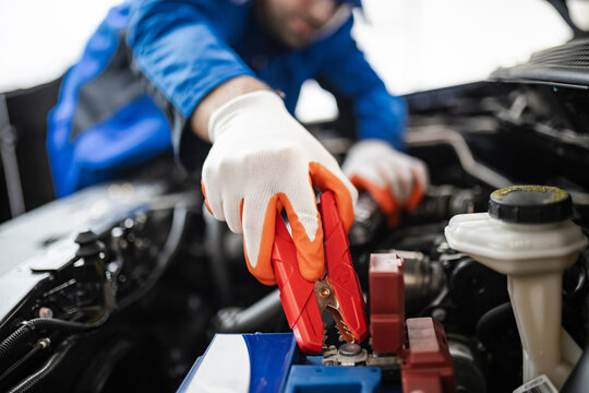 A mechanic using jumper cables to start a car battery in a workshop during daytime