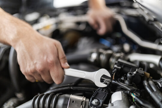 A mechanic using a wrench to repair an engine in an automobile workshop during daytime