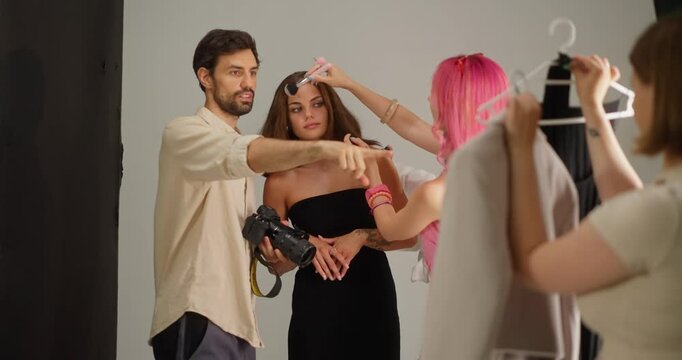 Confident guy brunette cameraman chooses what clothes are best for a girl model while communicating with stylists and preparing for photography in a modern studio