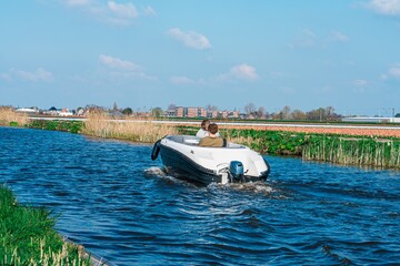 Two friends are enjoying chatting while boating on a river surrounded by green fields. There are...