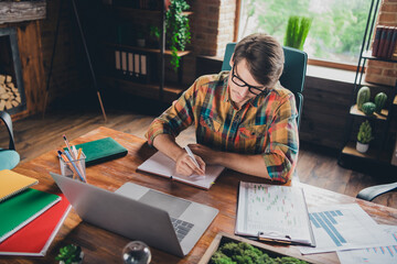 Photo of young man wear checkered shirt sit table at workplace write plan schedule task notes...