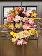 Autumn wreath hanging on brown wooden door with window. 