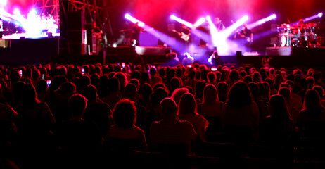 audience members viewed from behind during a live concert with stage lights shining on performing...