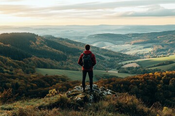 Fototapeta premium A hiker with a yellow backpack standing on a mountain peak, overlooking a scenic valley with winding river, nature exploration