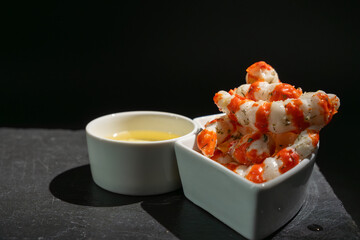 Next to it is a plate of Surimi in the form of shrimp on a black stone with a dipping sauce. The...
