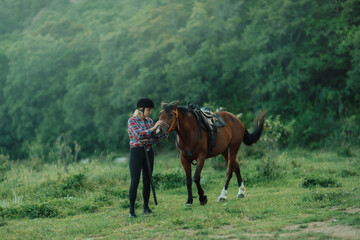 Happy blonde with horse in forest. Woman and a horse walking through the field during the day. Dressed in a plaid shirt and black leggings.