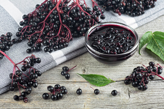 Fresh ripe black elderberries, elderberry syrup and leaves of elderberry on rustic wooden boards background. Alternative medicine and lifestyle.