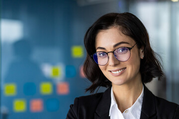 Confident businesswoman in glasses smiles in office setting. Professional appearance suggests...