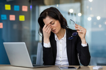 Stressed businesswoman in office feels fatigue, holding glasses, rubbing forehead. Overworked...