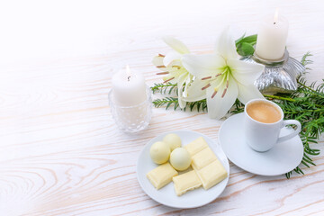 Winter holiday dessert with white chocolate, lilies, candles and coffee cup on a light background wooden, festive Advent and Christmas celebration, copy space, selected focus