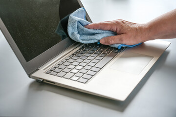 Hand cleaning a dusty laptop with a blue cloth, hygiene at the workplace maintains health, especially with frequently used devices, copy space, selected focus